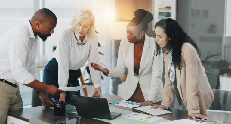 Team members crowded over a table going over reports in the office.